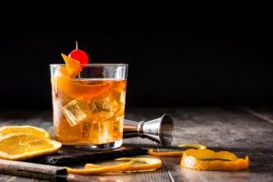 An old fashioned cocktail with a cherry and orange peels.